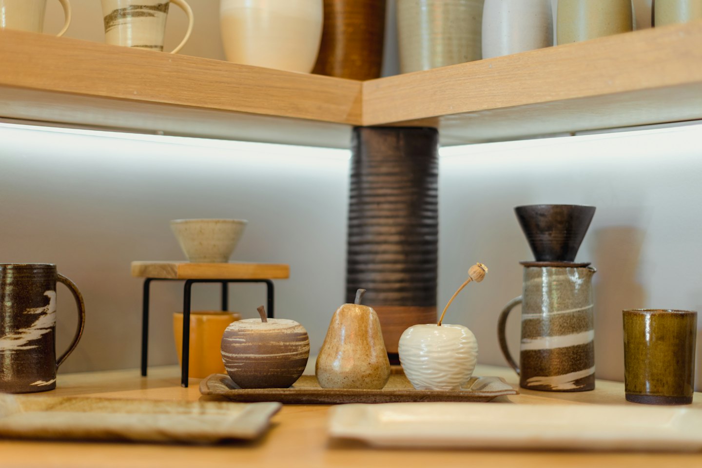 Ręcznie robione ceramiczne kubki i miski ułożone na drewnianych półkach.
