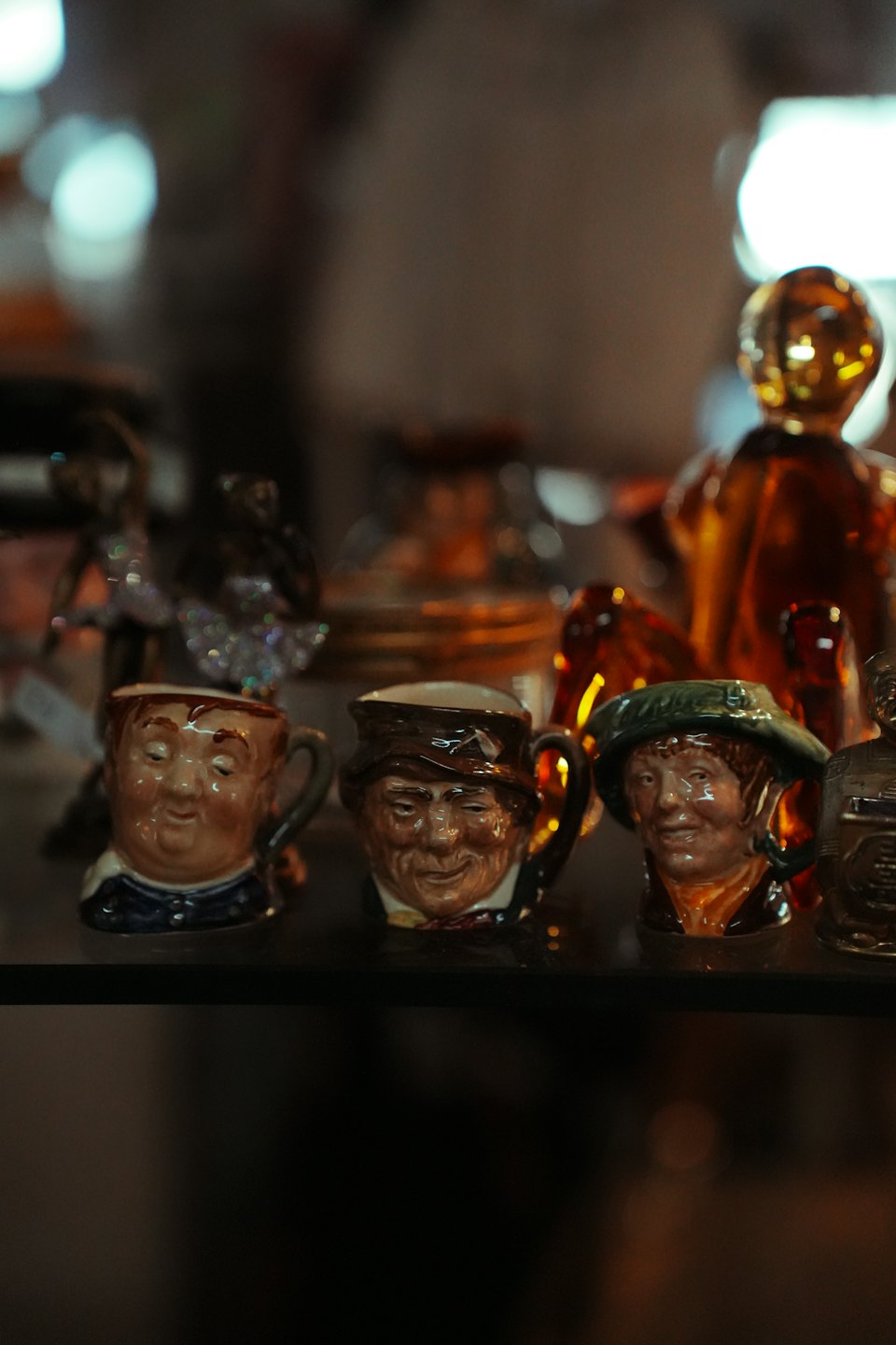 Trzy ceramiczne kubki w kształcie twarzy stojące na szklanej półce ekspozycyjnej.
