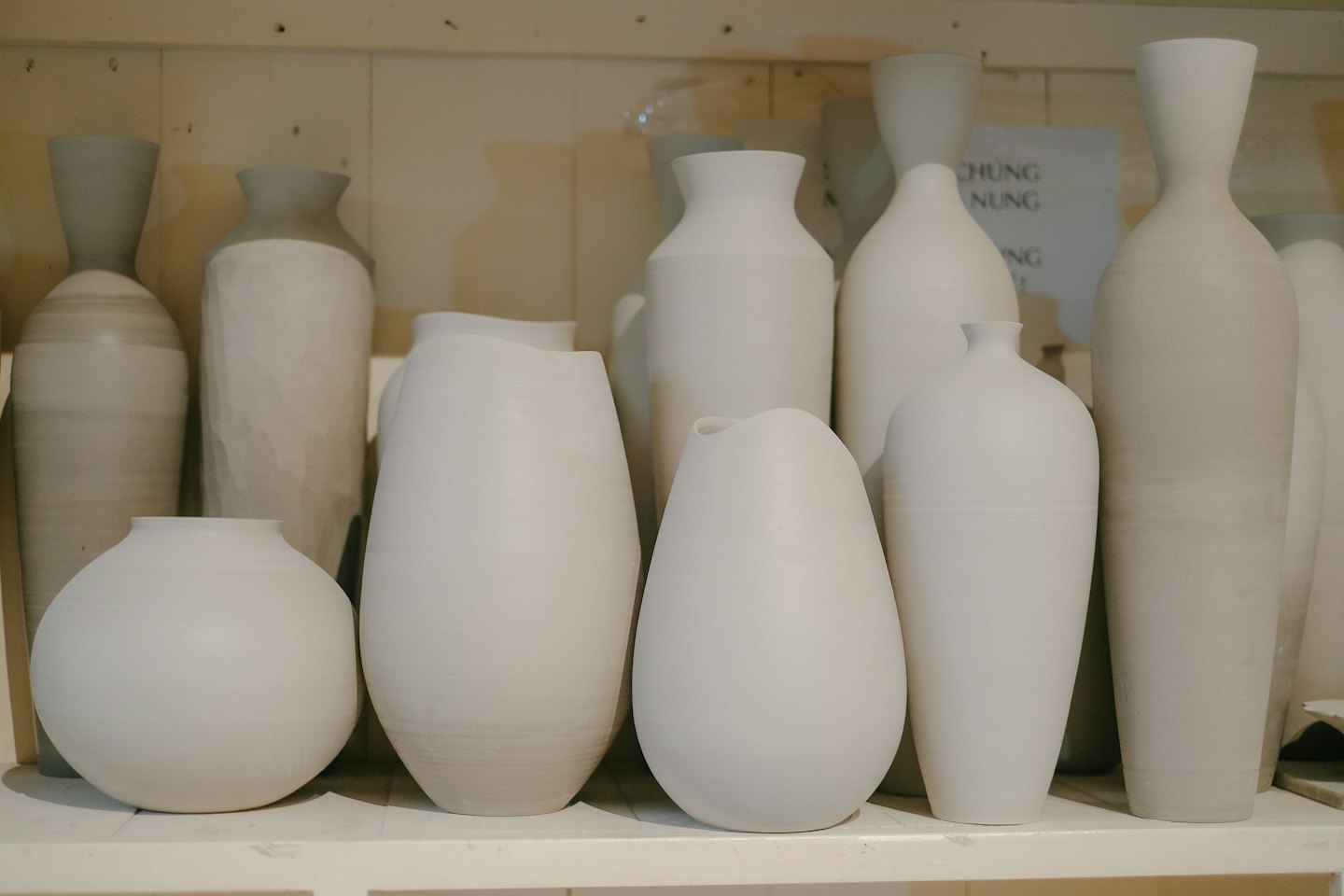 Nieniklowane ceramiczne wazony i doniczki o różnych kształtach na drewnianej półce.